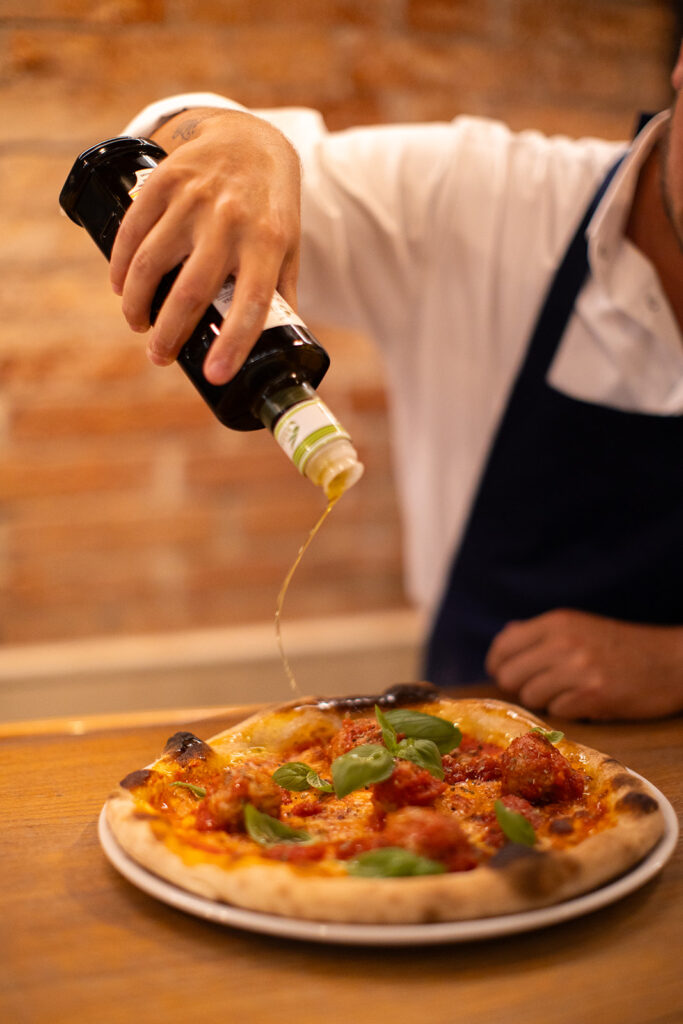 Un cameriere che versa dell'olio in una pizza margherita